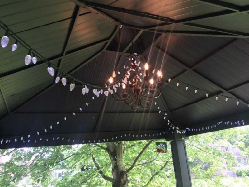 A chandelier hangs inside a dark gazebo with strings of white fairy lights illuminating the ceiling.