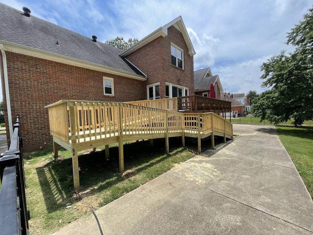 A newly constructed wooden wheelchair ramp with railings attached to the side of a brick house next to a concrete driveway.