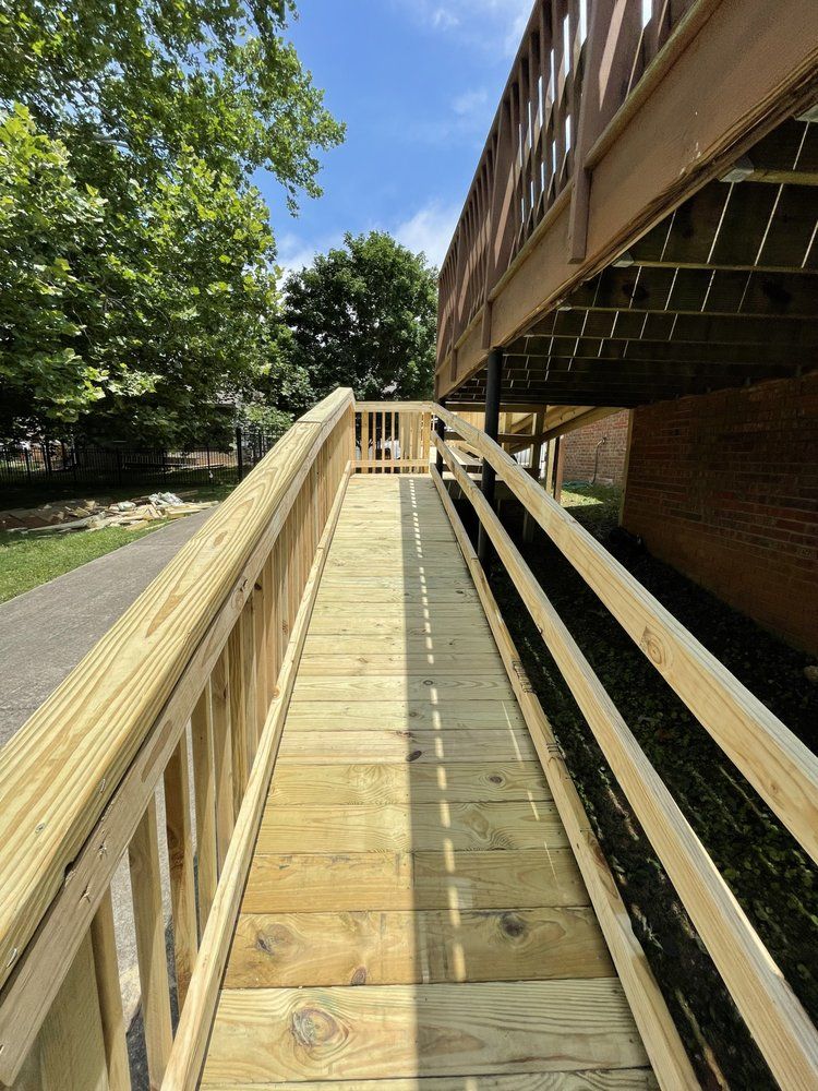 A wooden wheelchair ramp leading up to a raised deck alongside a brick building and a paved path.