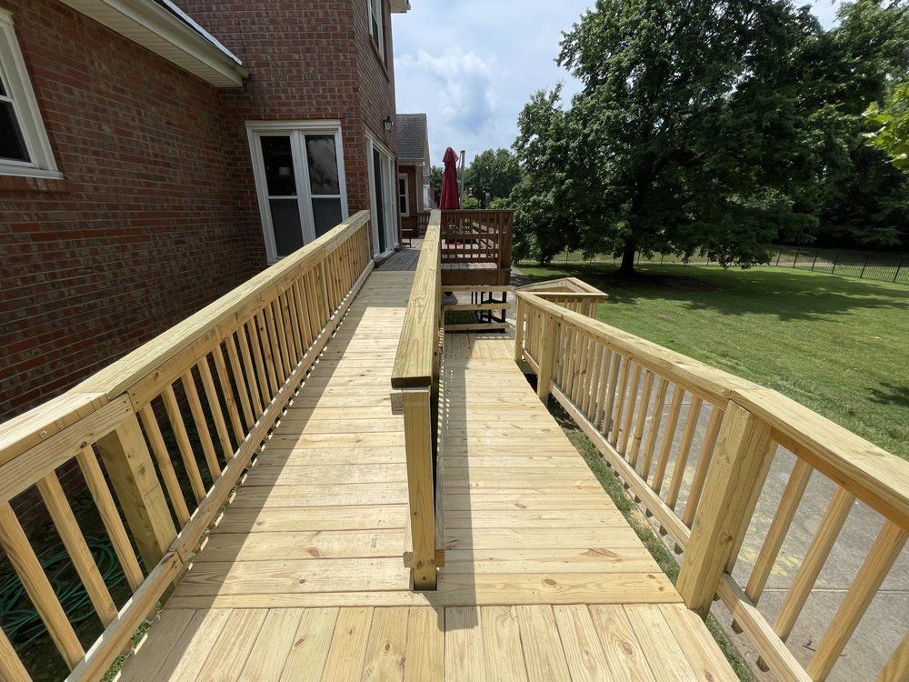 Newly constructed wooden wheelchair ramp with railings extending along the side of a brick house toward a backyard.