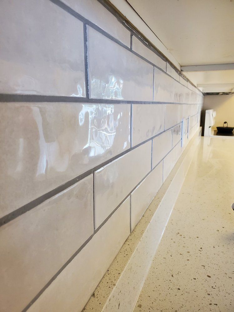 A close-up, angled view of a white, glossy rectangular tiled backsplash above a speckled countertop.