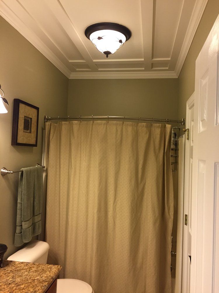 A bathroom interior with sage green walls, a beige shower curtain, a granite countertop, and a decorative coffered ceiling.
