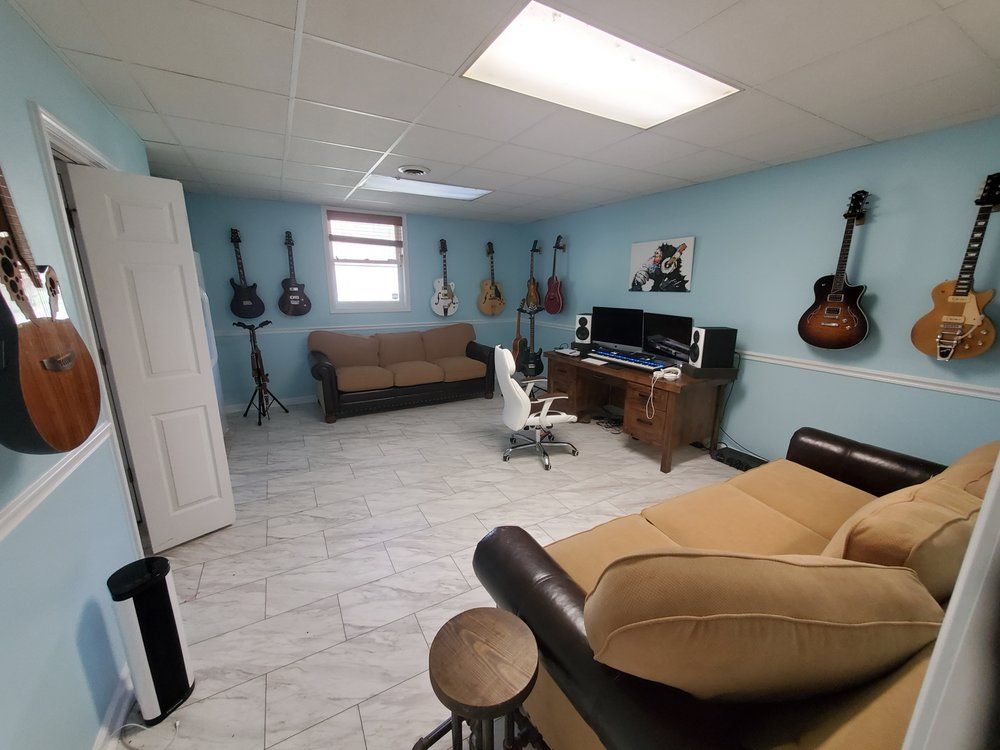 Music studio with light blue walls, tiled floors, two brown couches, a computer desk, and multiple guitars on the walls.