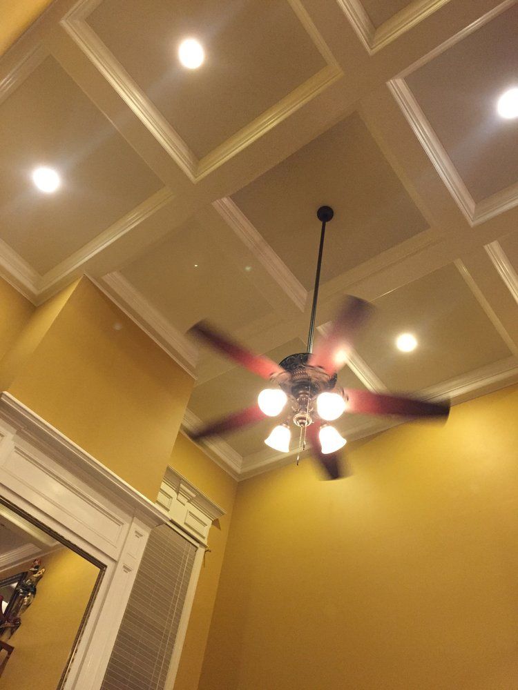 A ceiling fan with lights spinning in a room with a gold-colored coffered ceiling and recessed lighting.