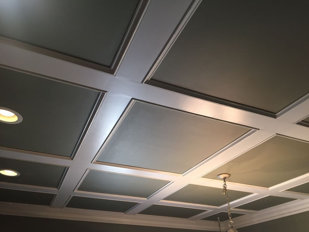 A coffered ceiling with white grid beams contrasting against square, sage-green recessed panels and recessed lighting.