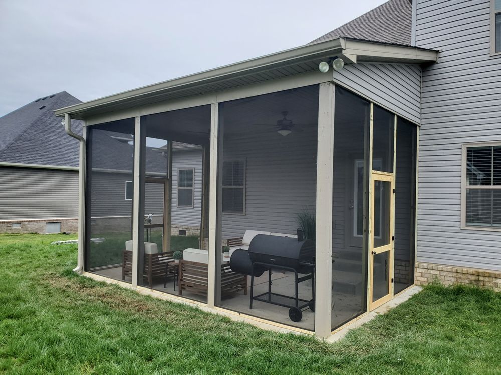A screened-in patio attached to the back of a house, featuring outdoor furniture, a grill, and a wooden screen door.