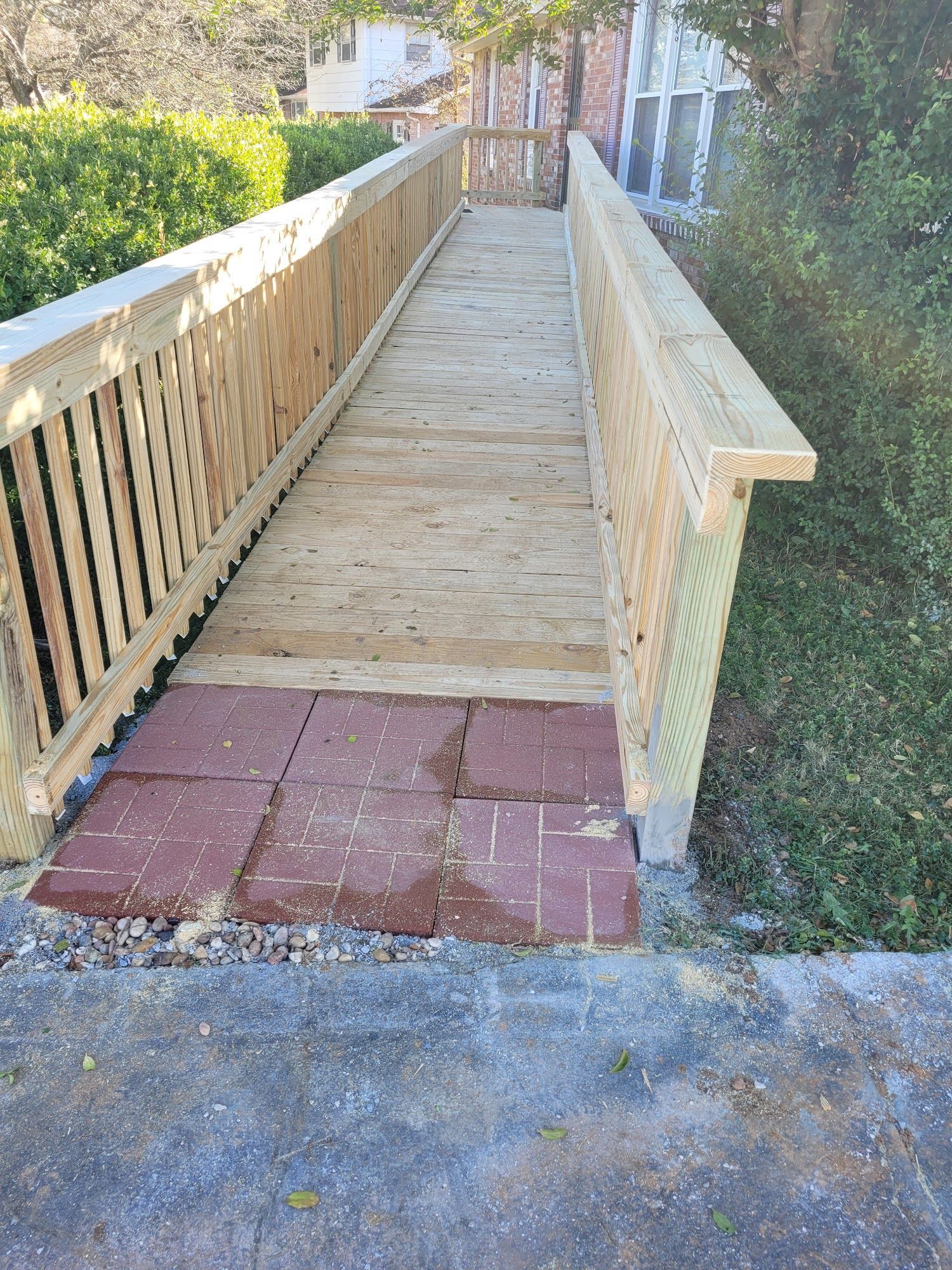 A wooden wheelchair ramp leading up to a building, with a transition of red brick pavers at the base.