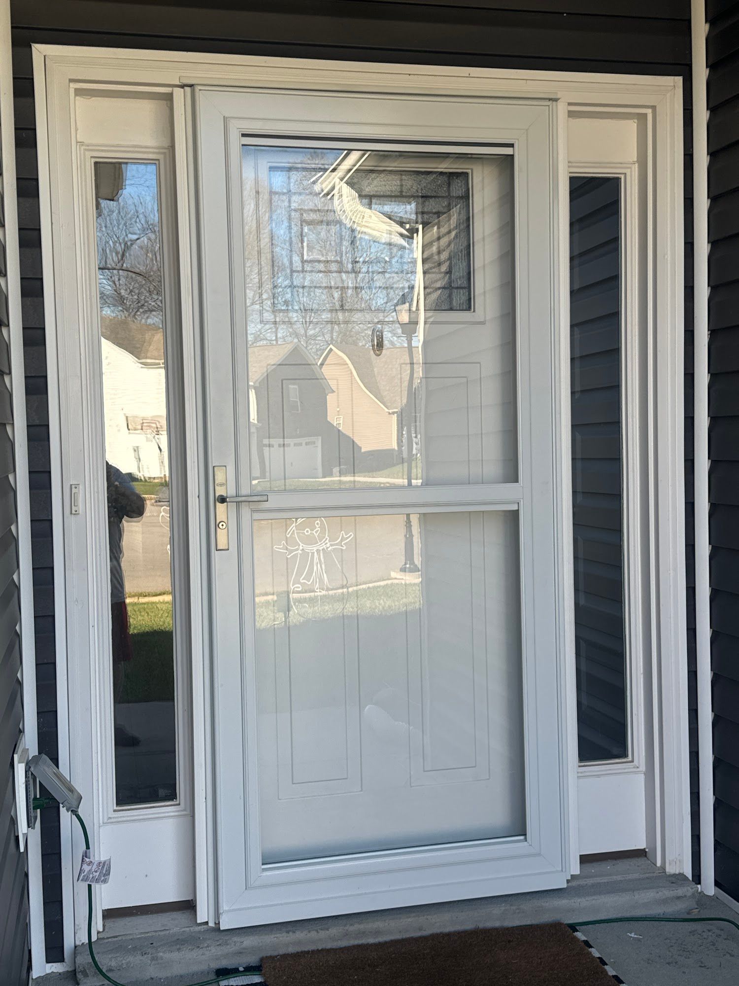A white storm door with glass panels installed over an entry door, framed by two sidelights against dark gray siding.