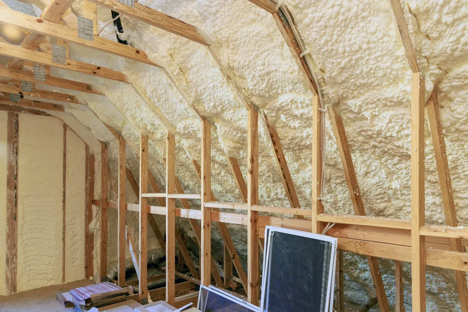An unfinished attic space showing wooden rafters and wall studs insulated with yellow spray foam insulation.