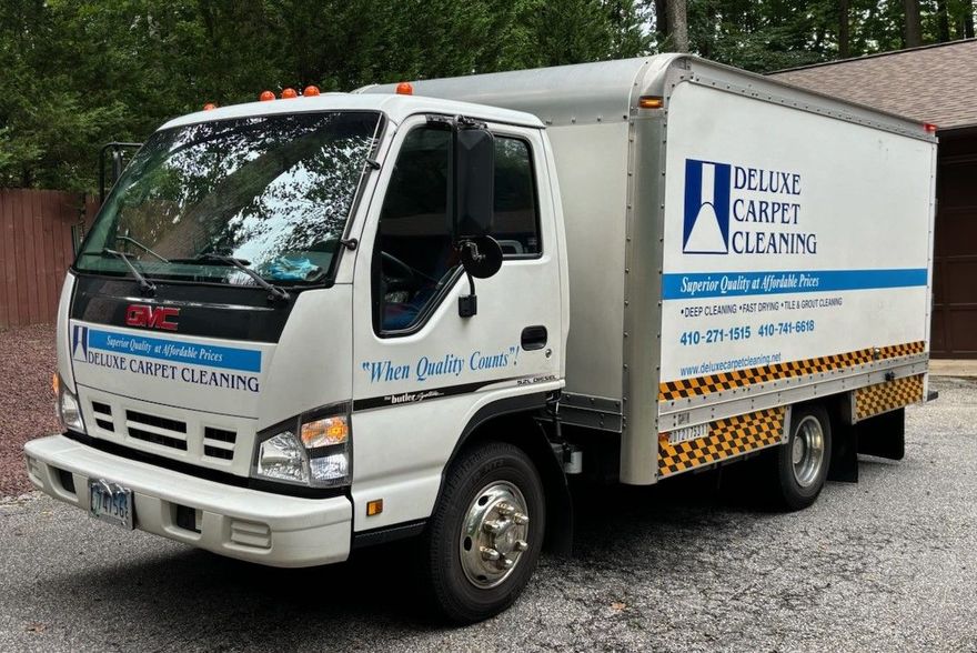 White delivery truck with blue lettering parked on gravel, side and front view.