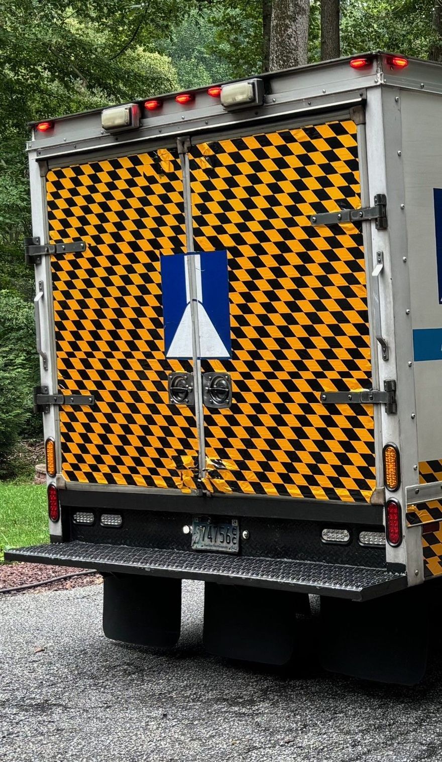 Rear of a truck with black-and-yellow chevron doors and red lights parked on a wet road.