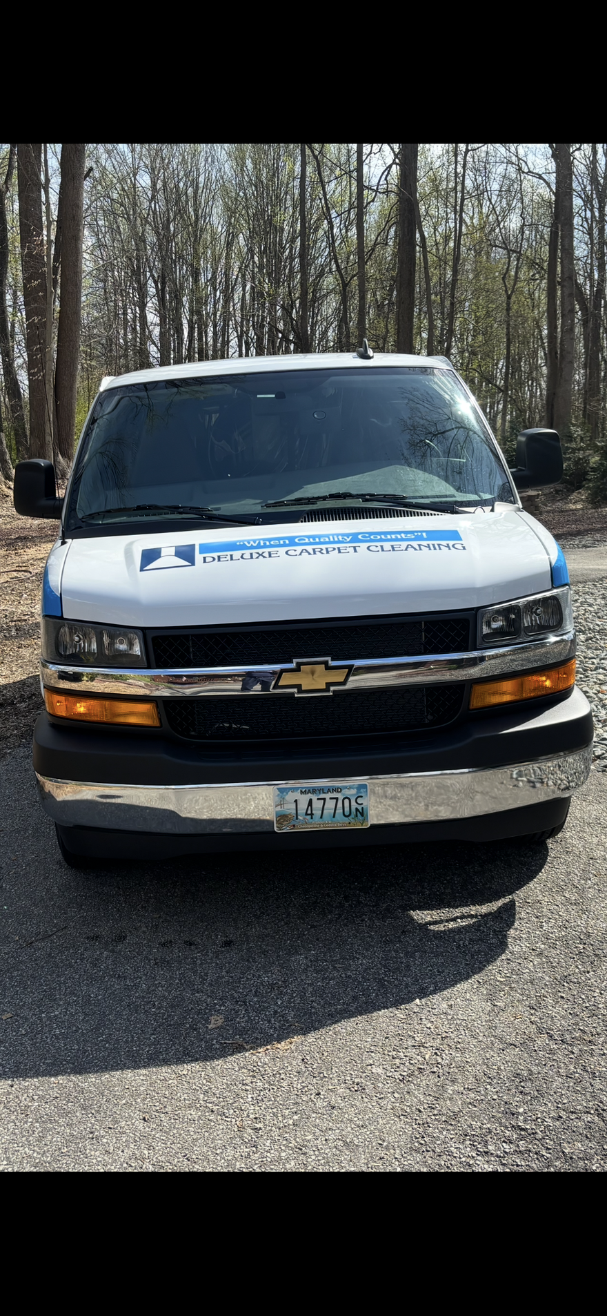 Front view of a white Chevrolet utility vehicle parked on a gravel road in a wooded area.