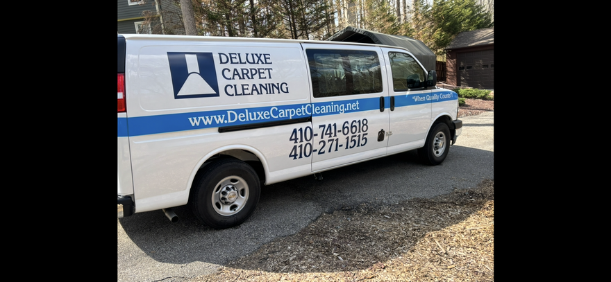 White Deluxe Window Cleaning van parked on gravel, with blue logo and phone number on the side.