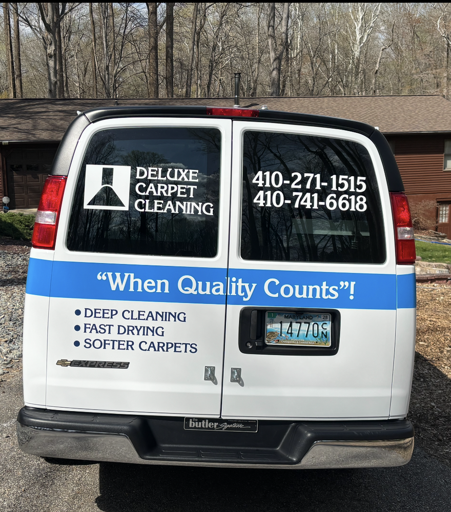 White van with “Deluxe Carpet Cleaning” ads and phone numbers parked in a wooded area.