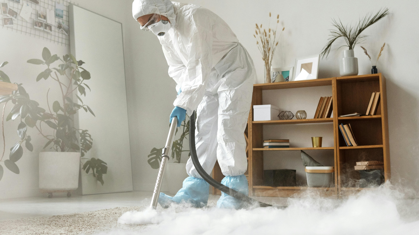 A man in a protective suit is cleaning the floor with a vacuum cleaner.