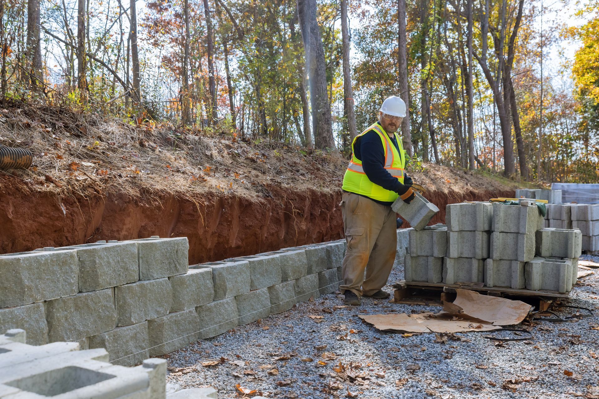 A construction worker is carrying a pallet of concrete blocks.