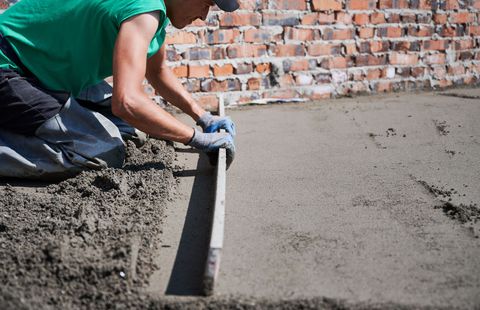 A man is laying concrete on the ground with a level.