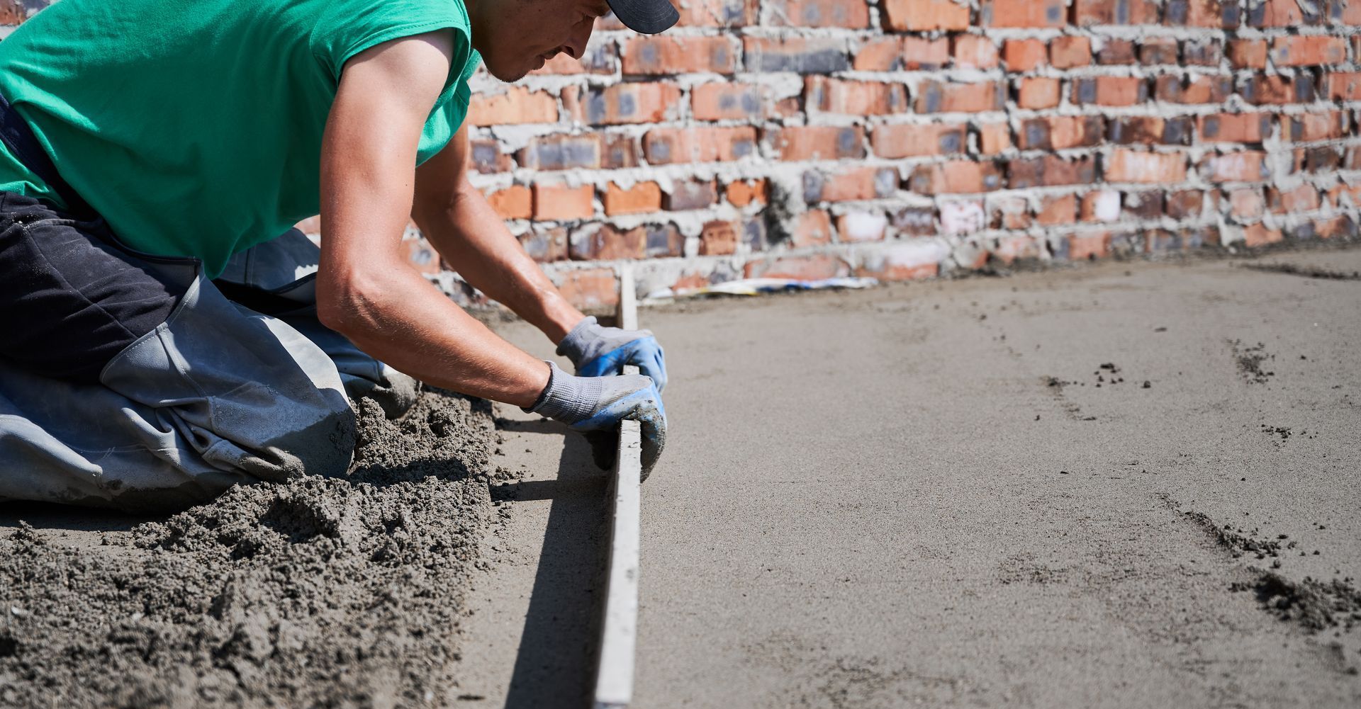 A man is kneeling on the ground using a level to level concrete.
