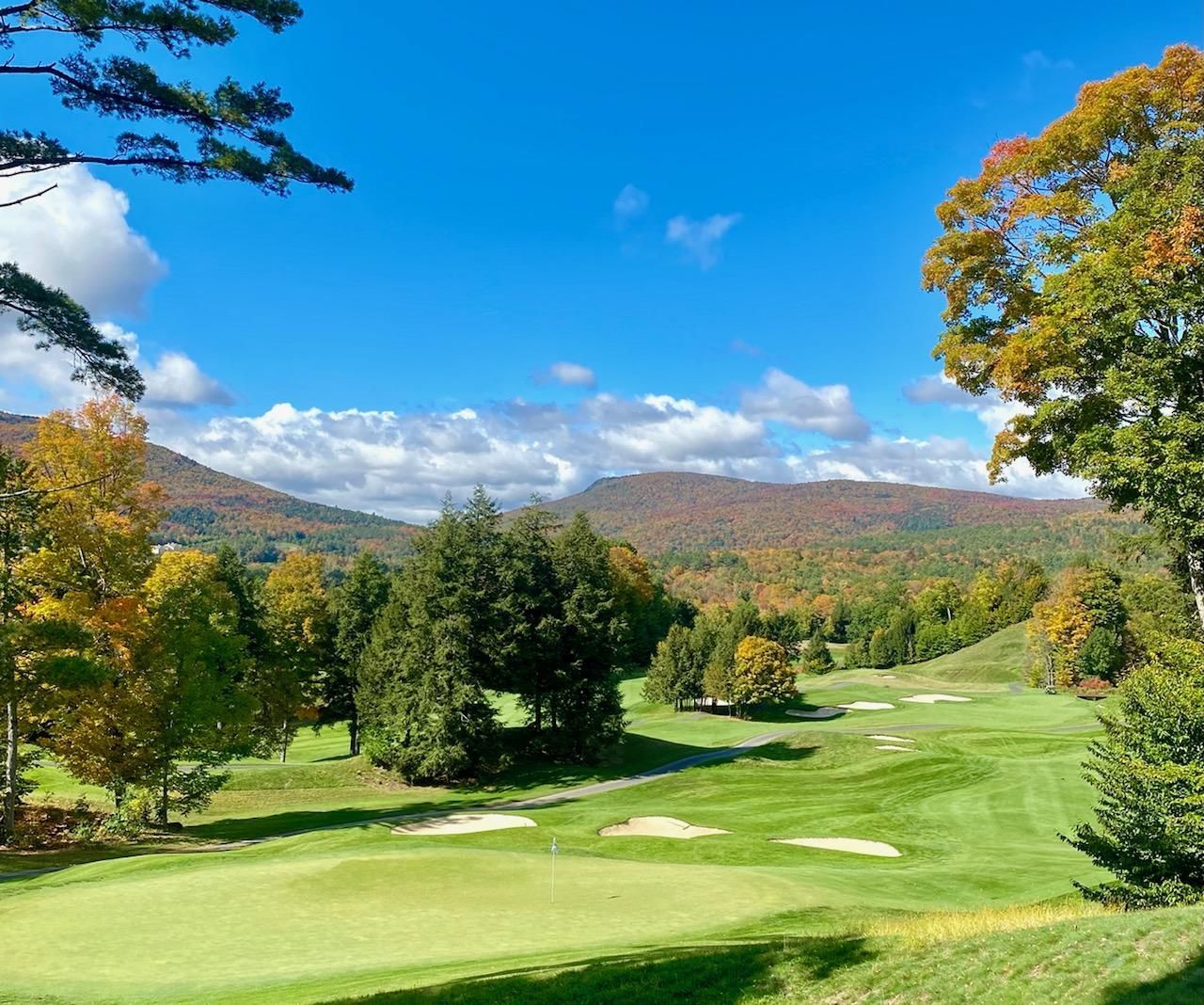 A golf course with trees and mountains in the background on a sunny day.