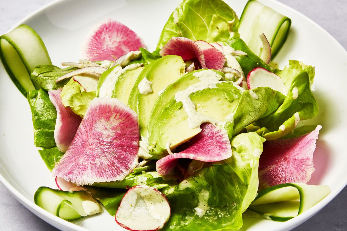 A salad with avocado , radishes , lettuce and cucumbers on a white plate.