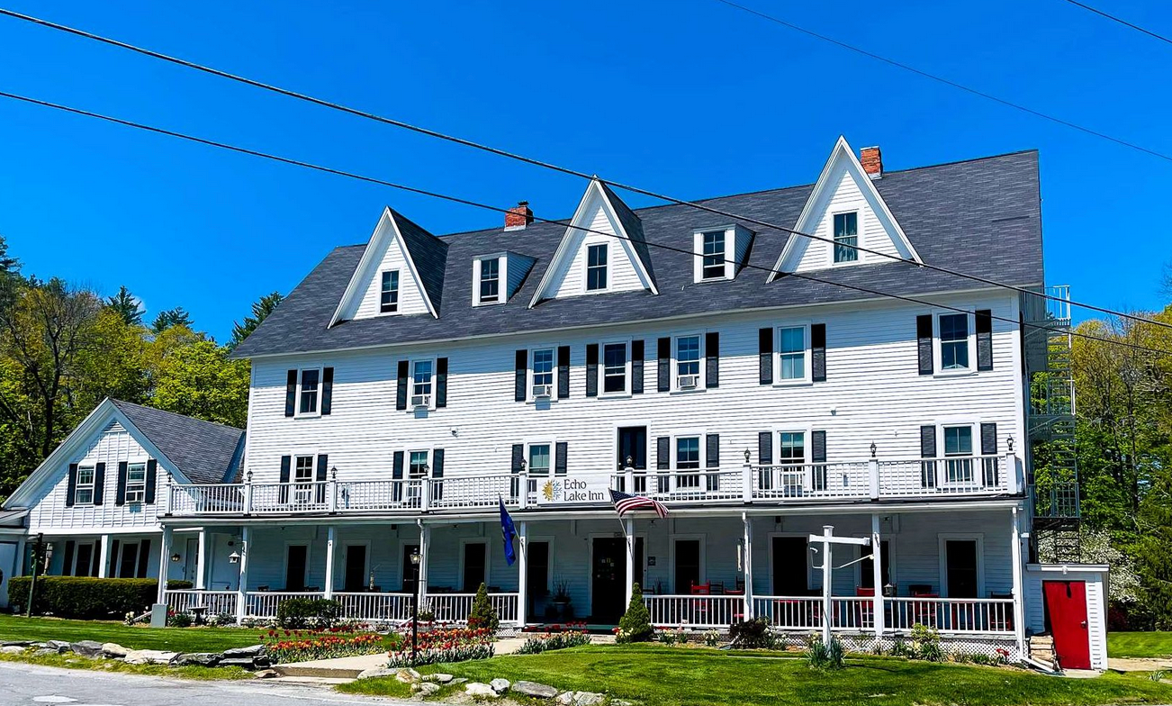 A large white house with a gray roof and a large porch.