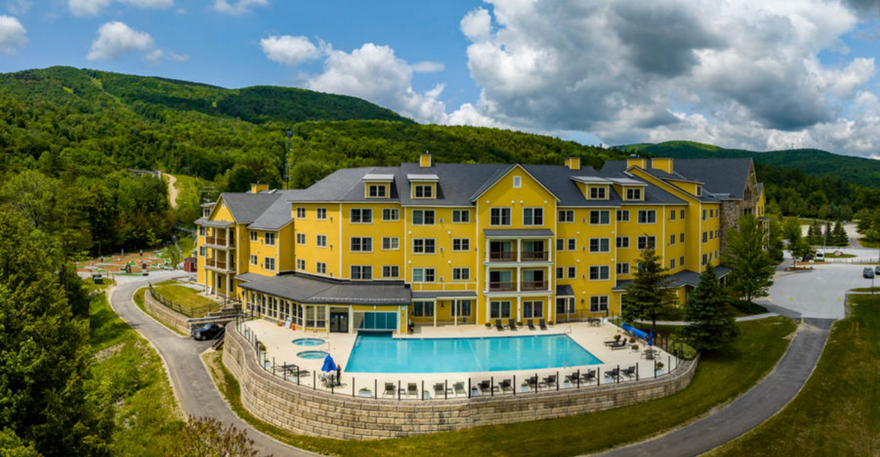 An aerial view of a large yellow building with a swimming pool in front of it.