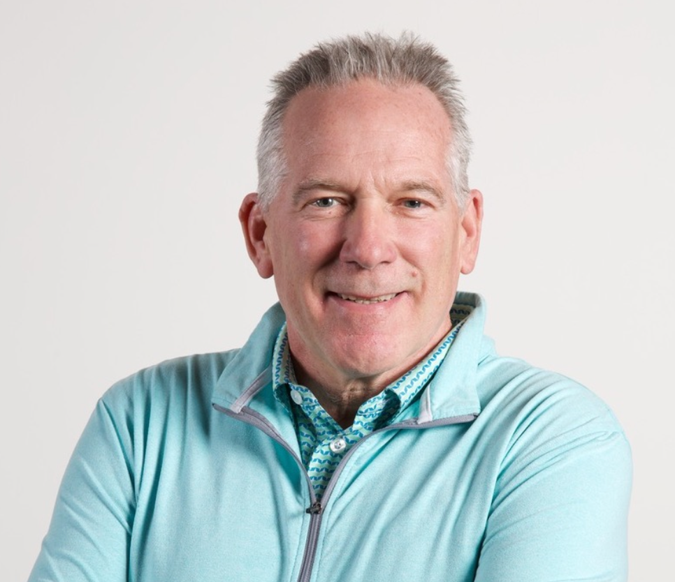 A man wearing a light blue jacket and a blue shirt is smiling for the camera.