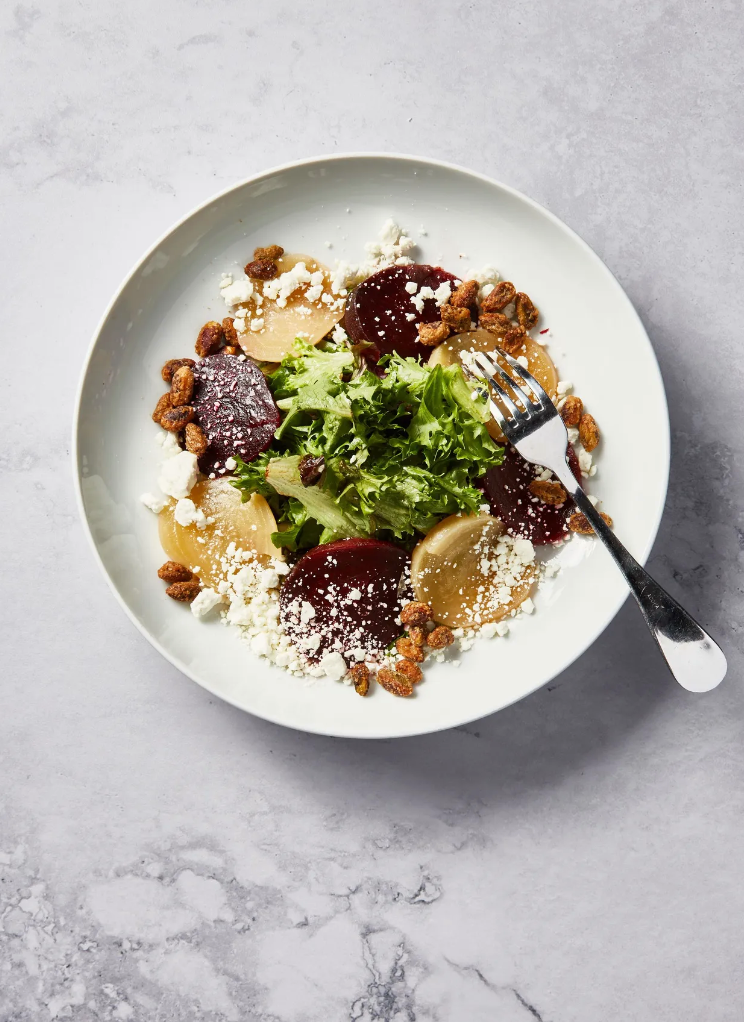 A white plate topped with a salad and a fork on a table.