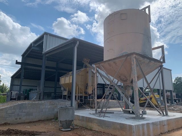 Industrial facility with a large metal silo and hopper under a partly cloudy sky