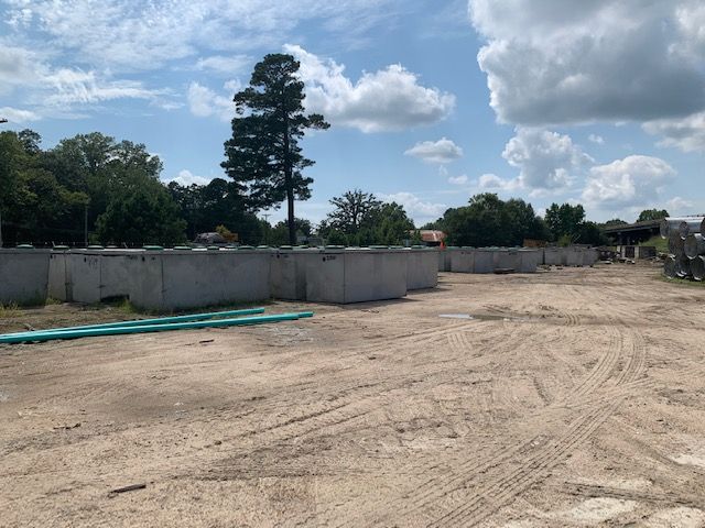 Empty dirt lot with low concrete walls, trees, and a cloudy sky