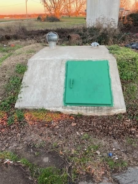 Small concrete utility hatch with green door in a grassy field at sunset