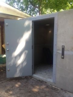 Open gray metal door on a concrete building, showing a dark interior.