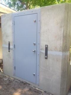 Gray metal door set in a concrete wall outdoors, with two vertical handles and multiple locks.