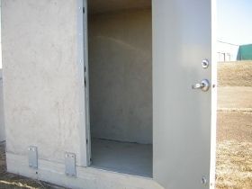 Open metal door on a concrete utility building, revealing a bare interior room.