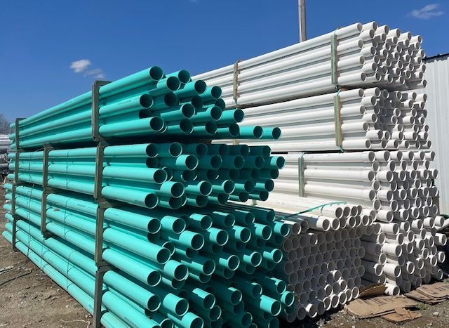 Stacks of turquoise and white PVC pipes stored outdoors under a blue sky.