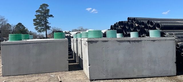 Stacks of concrete barriers and coiled black pipes outdoors under a blue sky.