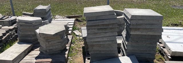 Stacks of gray paving slabs on wooden pallets outdoors in a yard