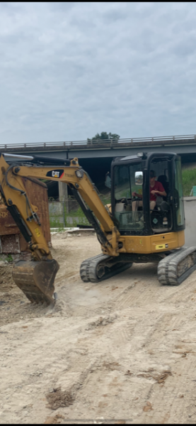 Yellow excavator on dirt road with a person inside, under a cloudy sky.