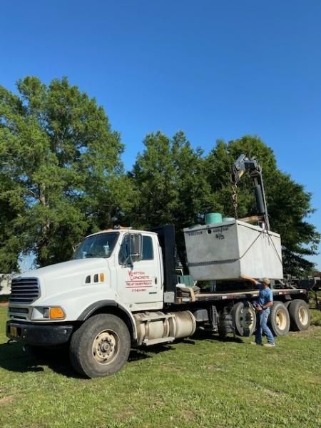 White utility truck with equipment trailer parked on grass under trees and a clear blue sky