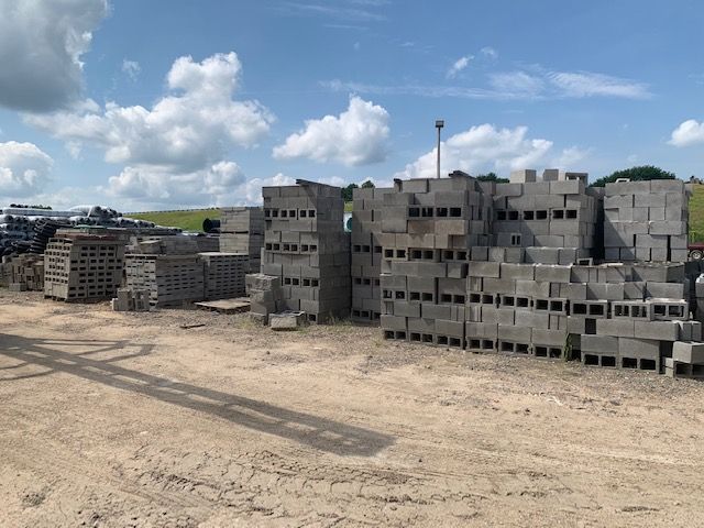 Stacks of gray cinder blocks on a sandy lot under a blue sky with clouds