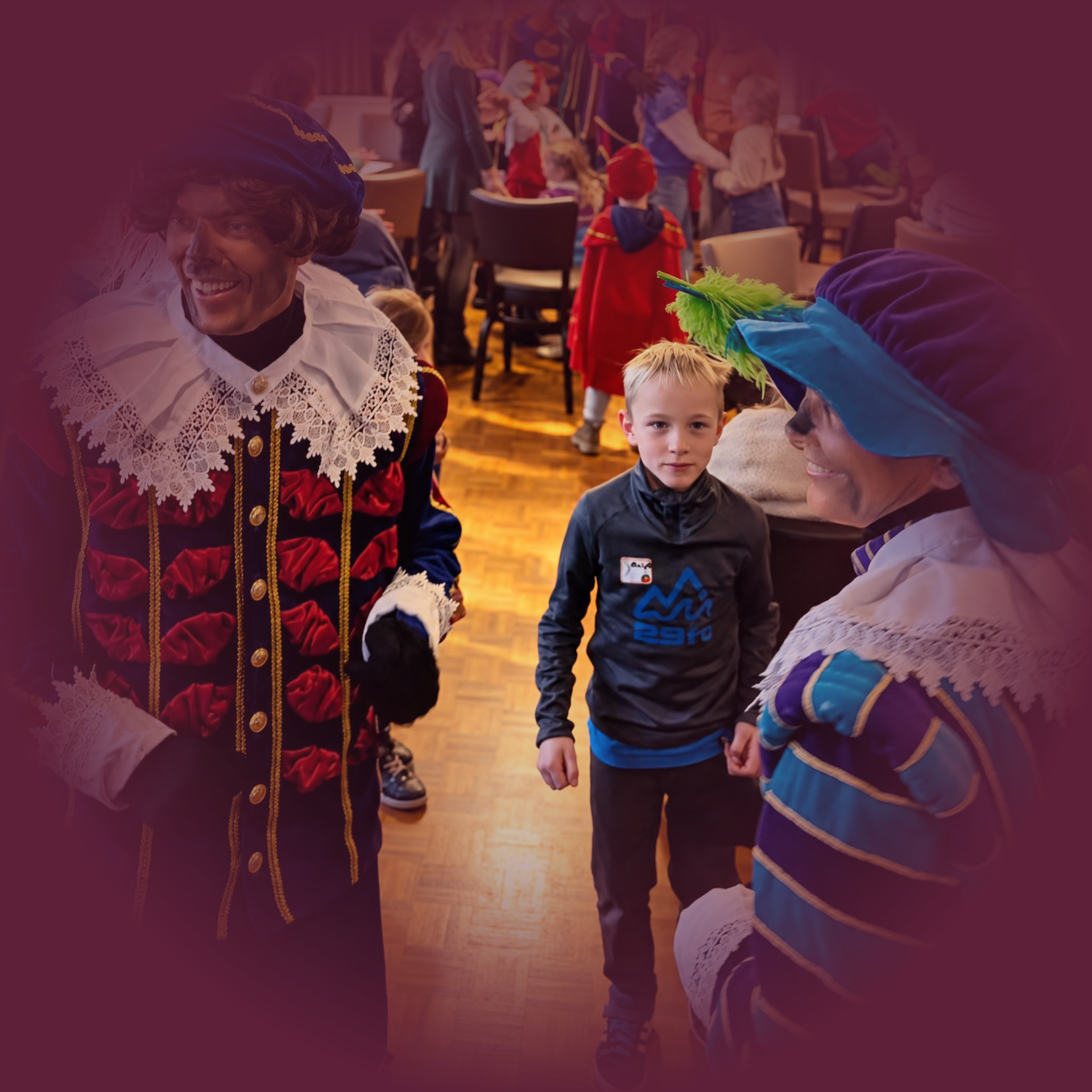 Kind staat tussen mensen in kleurrijke kostuums tijdens een feestelijk evenement binnenshuis.