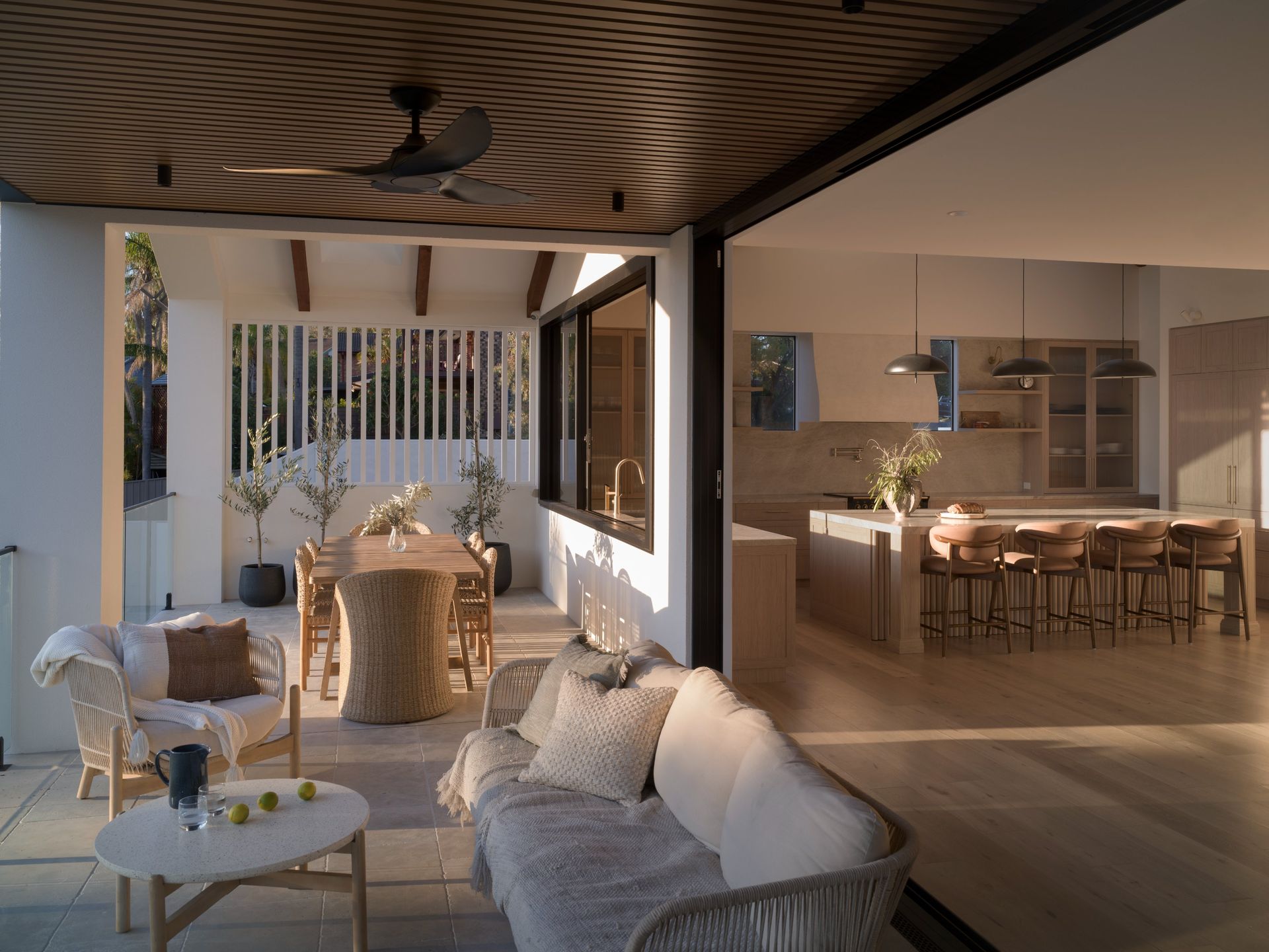 Open patio with woven seating and a table, overlooking a modern dining area with a long table and warm lighting  — Everyday Interiors in Wollongong, NSW