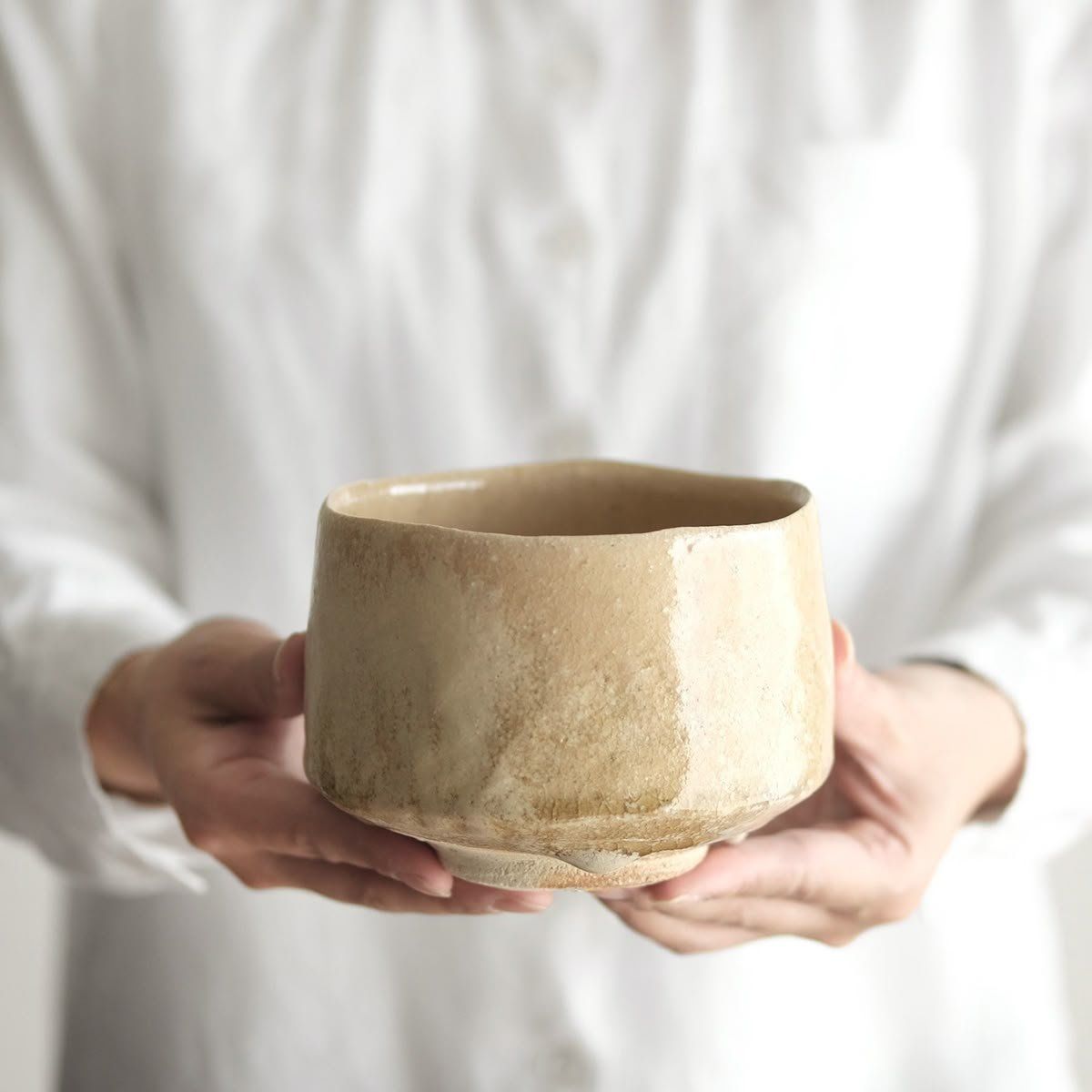 Hands Holding A Beige Ceramic Cup Against A White Shirt Background — Everyday Interiors in Helensburgh, NSW