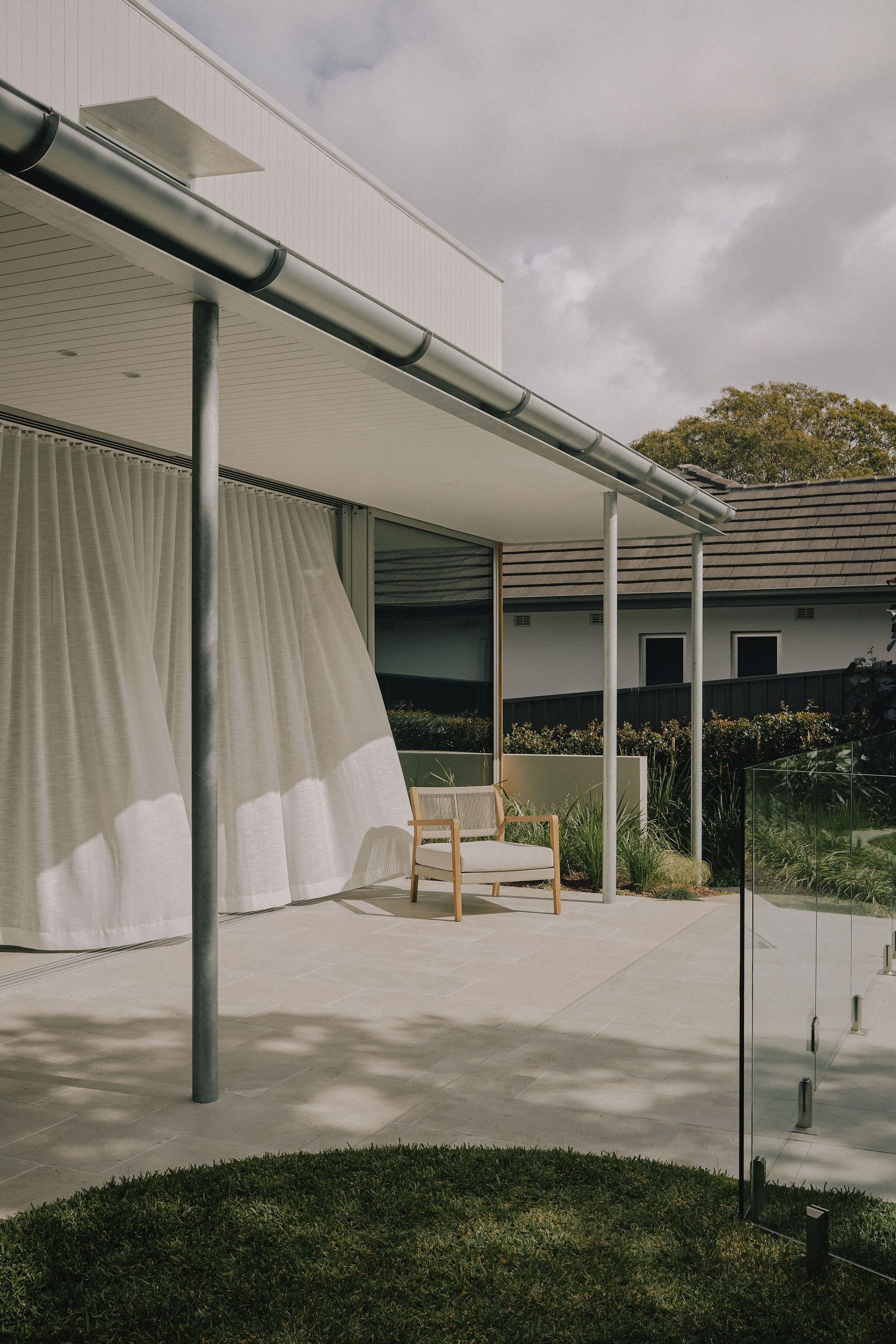Modern patio with white curtains, chairs, and a grassy yard under a cloudy sky — Everyday Interiors in Helensburgh, NSW