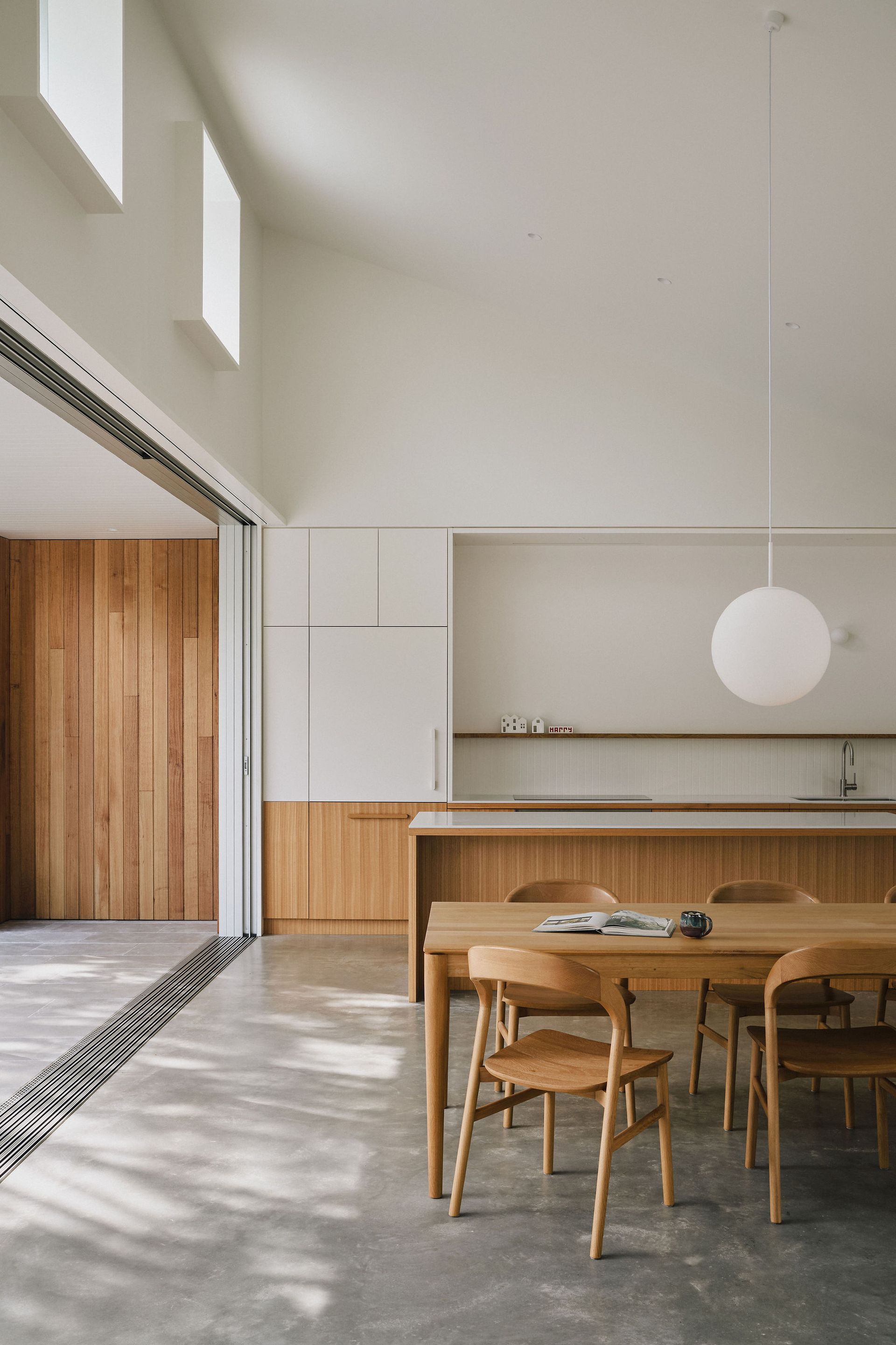 Bright minimalist dining room with wooden table, chairs, pendant light, and open kitchen/bar area — Everyday Interiors in Southern Highlands, NSW