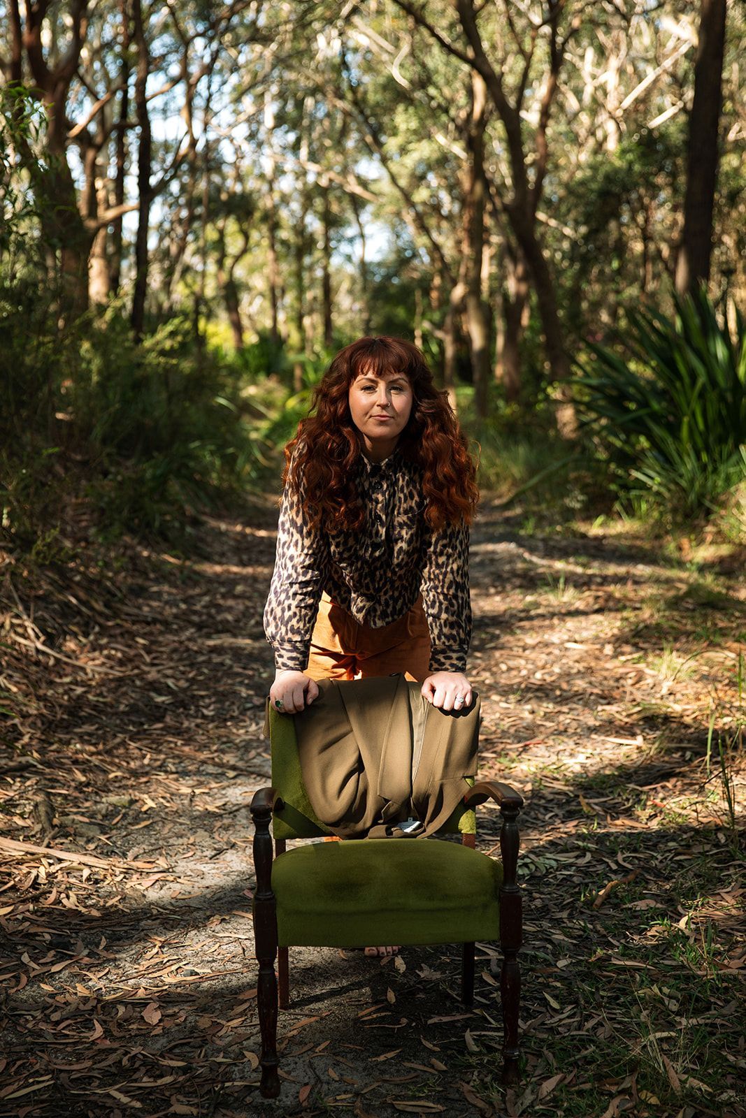 Woman with curly hair sitting on a green chair on a wooded path in dappled sunlight — Everyday Interiors in Helensburgh, NSW