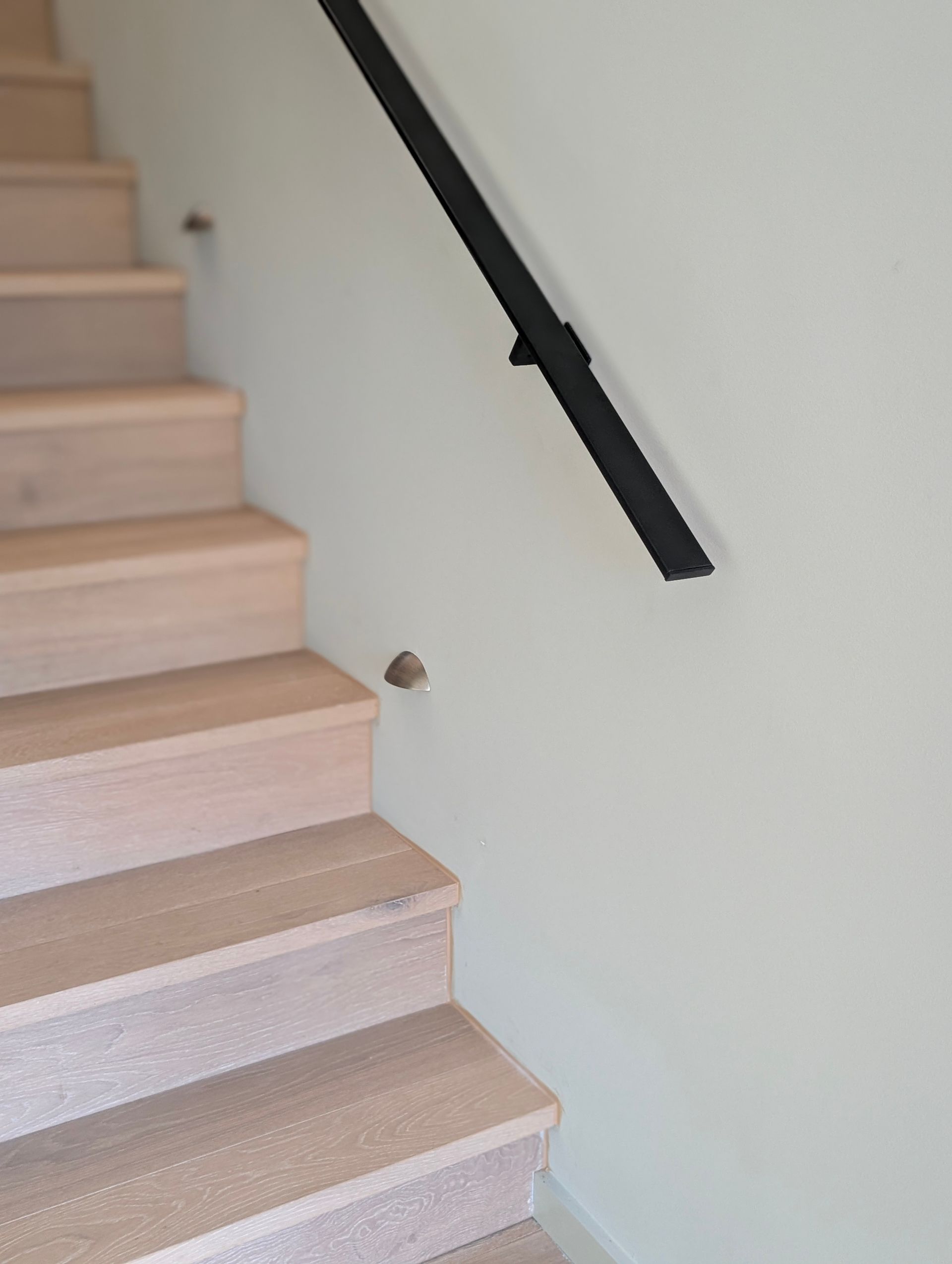 Indoor staircase with light wood steps, white wall, and black handrail — Everyday Interiors in Helensburgh, NSW