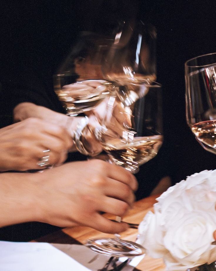 Hands Clink Wine Glasses At A Dimly Lit Table Beside A White Flower — Everyday Interiors in Helensburgh, NSW