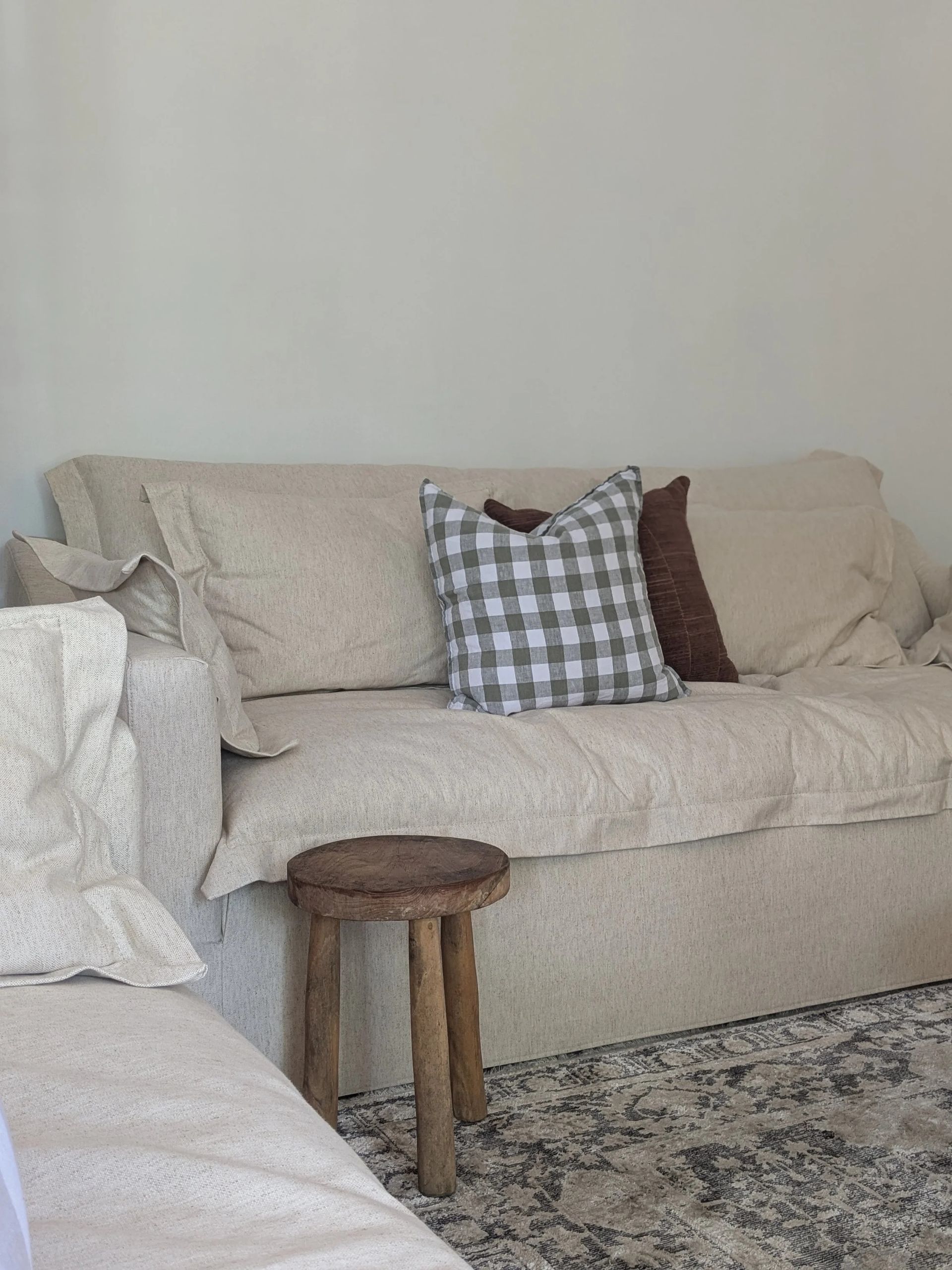 Cozy Living Room With A Beige Couch, Plaid Pillow And A Wooden Stool — Everyday Interiors in Helensburgh, NSW