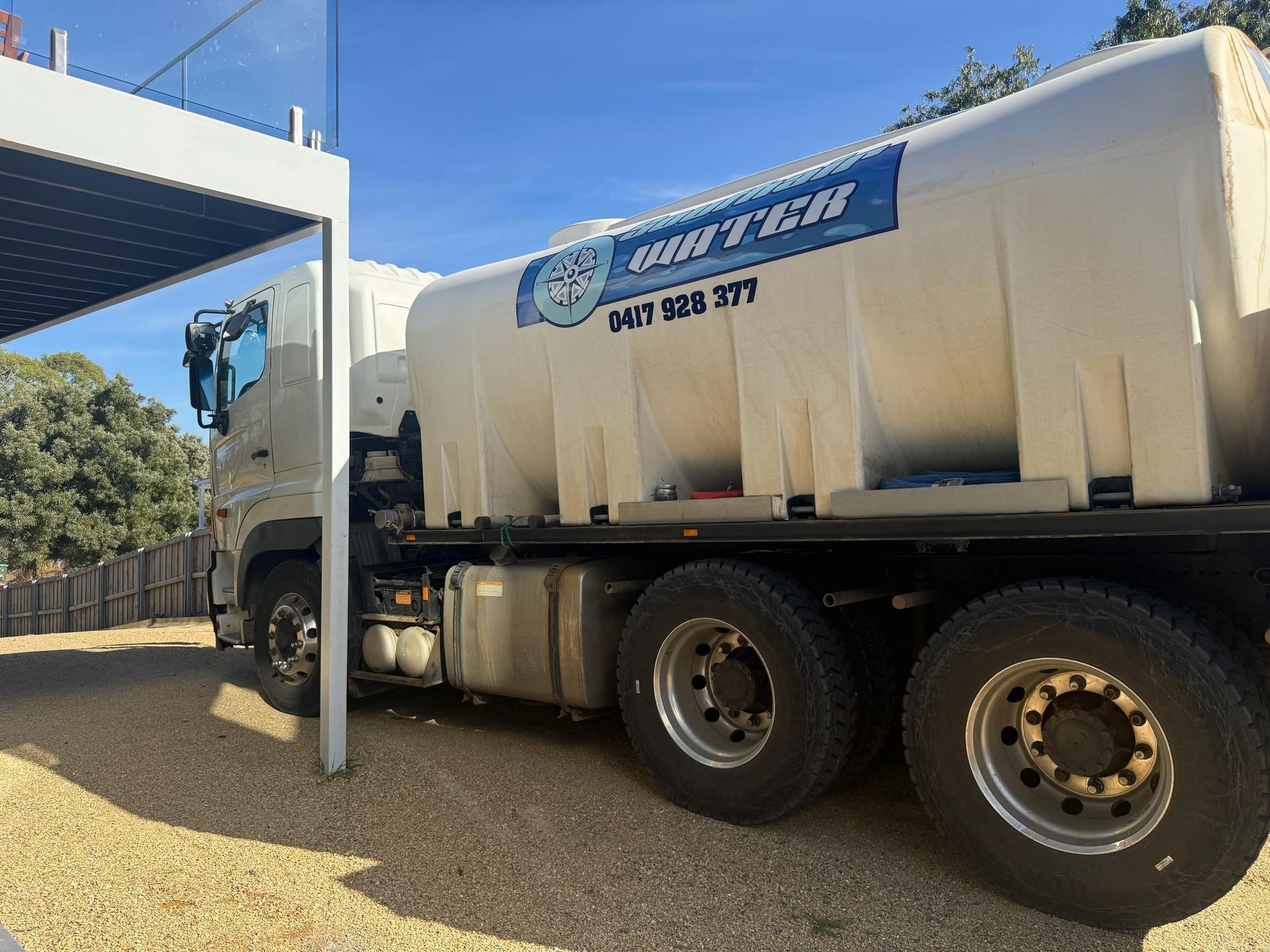 White tanker truck parked under a canopy on a sunny day